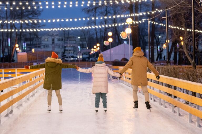 family skating together on an outdoor rink lit with string lights